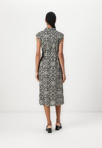 Rochie midi cu un model alb-negru, cu mâneci scurte tip capac, talie legată și siluetă dreaptă, prezentată din spate.