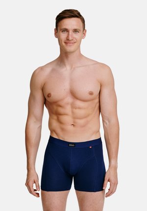 Boxer shorts blu navy con una texture morbida, vita elastica e dettagli di cucitura minimi. Il modello ha una fisicità muscolosa.