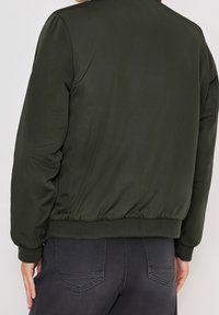 Veste bomber verte en tissu lisse, dotée de poignets et d'un ourlet côtelés, avec une coupe décontractée et une légère brillance.
