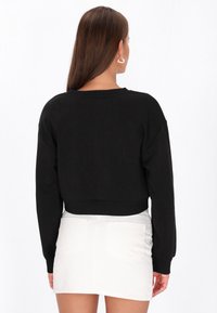 Fekete, rövidített pulóver hosszú ujjakkal és kerek nyakkivágással, fehér miniszoknyával párosítva. Sima textúra, egyszerű kialakítás.