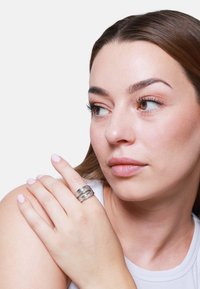 Anello d'argento composto da tre bande lisce e intrecciate. La superficie ha una finitura lucida con riflessi sottili. Il modello lo indossa su un dito.