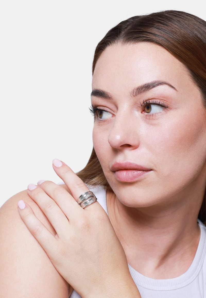 Anello d'argento composto da tre bande lisce e intrecciate. La superficie ha una finitura lucida con riflessi sottili. Il modello lo indossa su un dito.