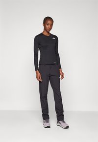 Maglietta nera a maniche lunghe e pantaloni neri in tessuto leggero, con il logo The North Face. Le calzature sono grigie con accenti neri.