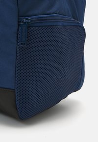 Mochila azul marinho com um painel em rede e base preta contrastante, apresentando um fecho de correr e um tecido texturizado para durabilidade.