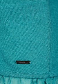 Tealtröja med en slät stickad textur, med en svart metall Esprit-logotyp på fållen och ett lager med volangdetalj i botten.