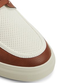 Bruna och krämfärgade sneakers med perforerat läder, rund tå, tjock sula och textilrem. Ytan är slät med synliga sömmar.