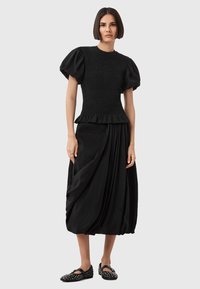 Vestito nero con top arricciato, maniche a sbuffo e gonna drappeggiata. Tessuto liscio, lunghezza al ginocchio con dettagli arricciati, abbinato a scarpe nere decorate.