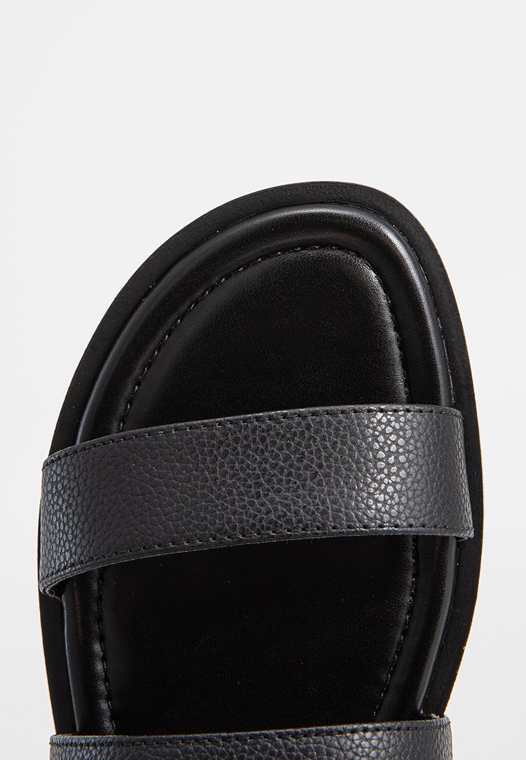 Sandalo in pelle nera con due larghe cinghie testurizzate, punta arrotondata e soletta liscia. La suola è leggermente sollevata.