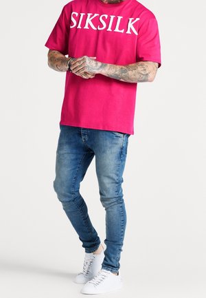 Magenta Baumwoll-T-Shirt mit "SIKSILK" in Weiß, kombiniert mit hellblauen Slim-Fit-Jeans und weißen Turnschuhen.