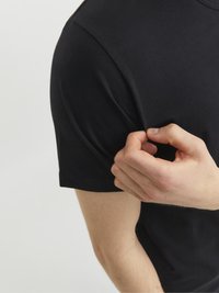 Schwarzes Baumwoll-T-Shirt mit kurzen Ärmeln, taillierter Passform und glatter Textur. Eine Hand zieht den Ärmel leicht, um die Flexibilität zu zeigen.