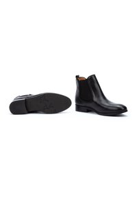 Las botas de cuero negro hasta el tobillo presentan un acabado suave, paneles laterales elásticos, una lengüeta de tirón y una suela de goma texturizada con un patrón sutil.