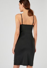 Robe nuisette en satin noir avec des fines bretelles ajustables, un design ajusté, longueur genoux, texture lisse et un minimum de détails.