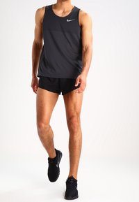 Débardeur de sport noir avec un logo Nike gris, associé à un short noir et des chaussures de course. Tissu lisse, design sans manches et coupe cintrée.