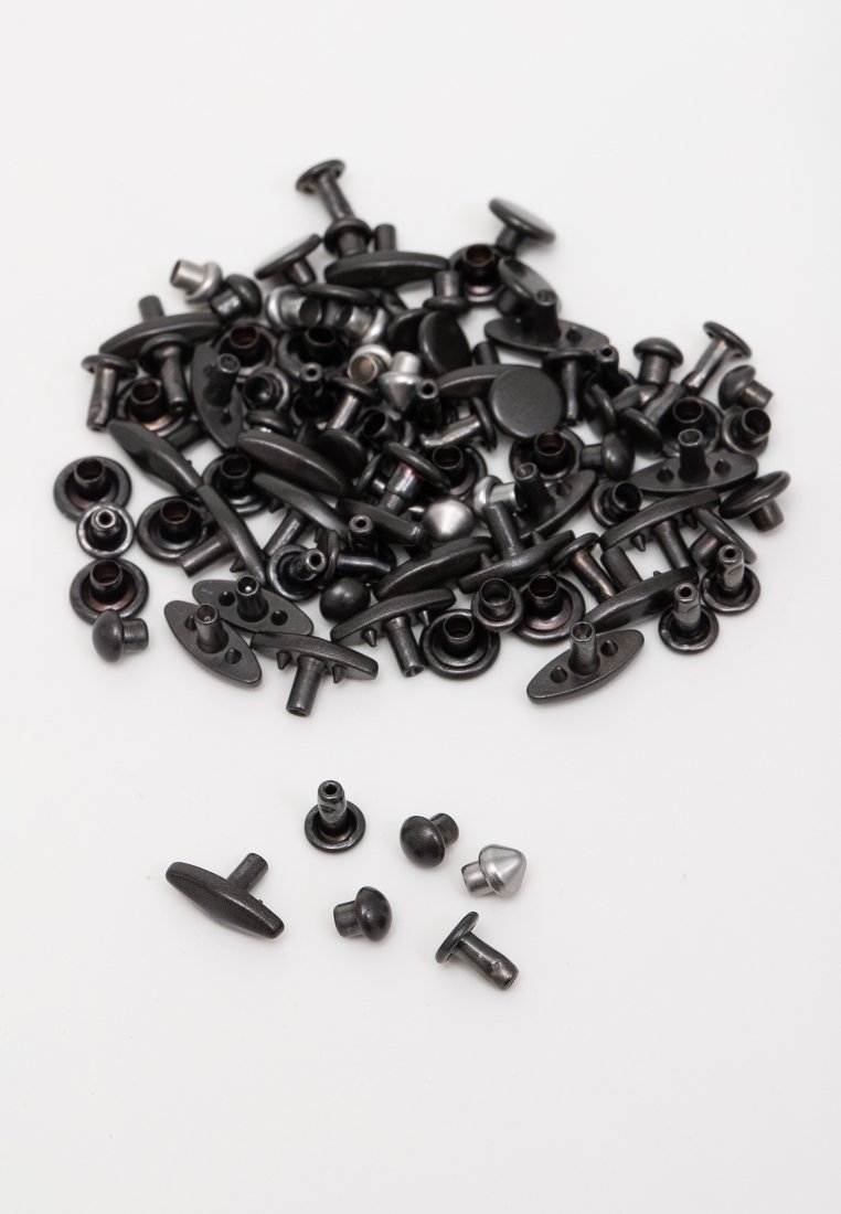 Mehrere schwarze und silberne Metallnieten und -verschlüsse, die auf einer weißen Fläche verteilt sind, wobei einige im Vordergrund getrennt sind.