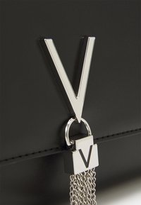 Borsa nera in sintetico con un grande logo 'V' argento, un dettaglio a catena attaccato da un anello, e cuciture pulite lungo i bordi.