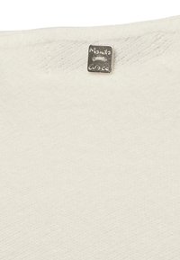 Tessuto strutturato color crema con un'etichetta argentata in rilievo con la scritta "Manila Grace" attaccata nella parte superiore, che presenta una forma rettangolare semplice.