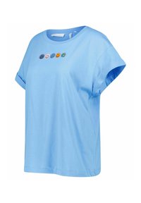 Ljusblå bomullströja med uppvikta korta ärmar, med fem flerfärgade broderade smiley-ansikten över bröstet.