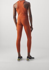 Top sportivo arancione e leggings, design attillato con texture liscia. Scarpe da corsa nere con suola bianca e accenti verdi.
