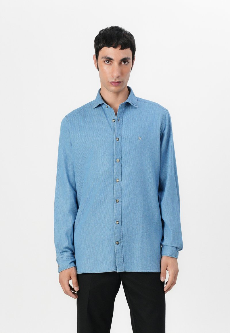 Camicia button-up a maniche lunghe di colore azzurro chiaro, in tessuto denim, con colletto a punta, taschino sul petto e dettagli di cuciture a contrasto.
