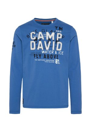 Camiseta de manga larga azul hecha de algodón. Presenta gráficos de texto en blanco y negro en negrita, cuello redondo y puños acanalados en las mangas.