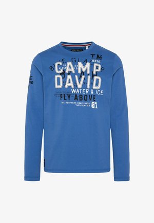 Camiseta de manga larga azul hecha de algodón. Presenta gráficos de texto en blanco y negro en negrita, cuello redondo y puños acanalados en las mangas.