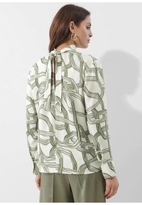 Langärmlige Bluse in Elfenbein mit grünen abstrakten Linien, ausgestattet mit einem Halsband-Detail und geknöpften Manschetten, aus einem glatten Stoff gefertigt.