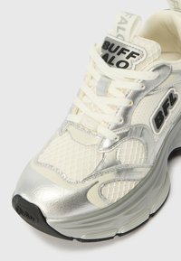 Hvite sneakers med mesh og metallisk sølvdesign. Har merkevare på tungen og siden. Teksturert hvit og sølv aksent. Svart yttersåle.