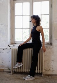 Black high-waisted trousers paired with a sleeveless black top and gray sneakers, positioned against a radiator by a window.