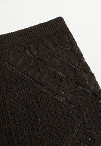 Gros plan sur un tissu en dentelle noire avec des motifs floraux et géométriques complexes et une bordure en maille côtelée.