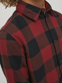 Camicia a quadri rossa e nera con colletto button-down, caratterizzata da una consistenza morbida e un design aderente, messa in risalto da colori a contrasto.