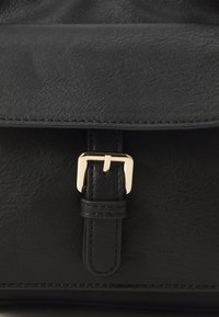 Black leather handbag with a smooth texture, featuring a flap closure and a gold-tone buckle accenting a central strap.
