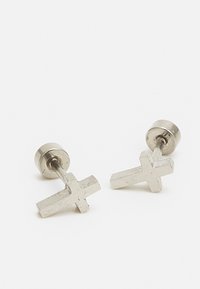 Brincos de estudo em tom prateado com um design de cruz. Acabamento em metal suave com uma forma minimalista e fecho seguro.