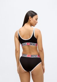 Conjunto de soutien desportivo preto e cuecas de corte alto, com detalhes em branco e faixas de logótipo Diesel em vermelho vivo nas bordas. Textura lisa e mate.