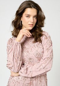 Rosa langärmliges Kleid mit aufwendigen Paillettenverzierungen. Fließender Stoff, strukturierte Ärmel und taillierte Korsage sorgen für eine elegante Silhouette.