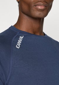 Tumši zila sporta krekls ar apaļu kakla izgriezumu, gludu tekstūru un smalku akcentu šuvi. Uz pleca ir "ICANIWILL" logo.