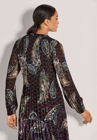 Lang, gemêleerd jurkje met een mix van paisley- en hartontwerpen in donkere kleuren. Plissé achterzijde en lange mouwen, met een ronde halslijn.