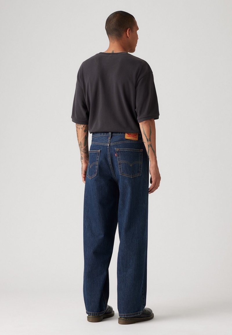 Dunkelgraues Oversize-T-Shirt kombiniert mit locker sitzenden blauen Jeans aus Denim, die Gesäßtaschen und ein hellbraunes Lederetikett aufweisen.