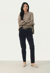 Beige knitted sweater with long sleeves, paired with dark navy corduroy pants and light beige flat shoes; model wears a black belt.