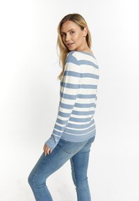 Randig tröja i ljusblått och vitt, med bred u-ringning och långa ärmar, ihopparad med åtsittande blå jeans, visad bakifrån.