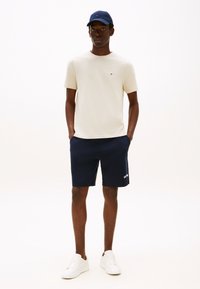 Beeźi t-särk, tumesinised lühikesed püksid, valged tossud ja tumesinine nokamüts. T-särgil on väike logo; lühikestel pükstel on küljel tekstidetail.