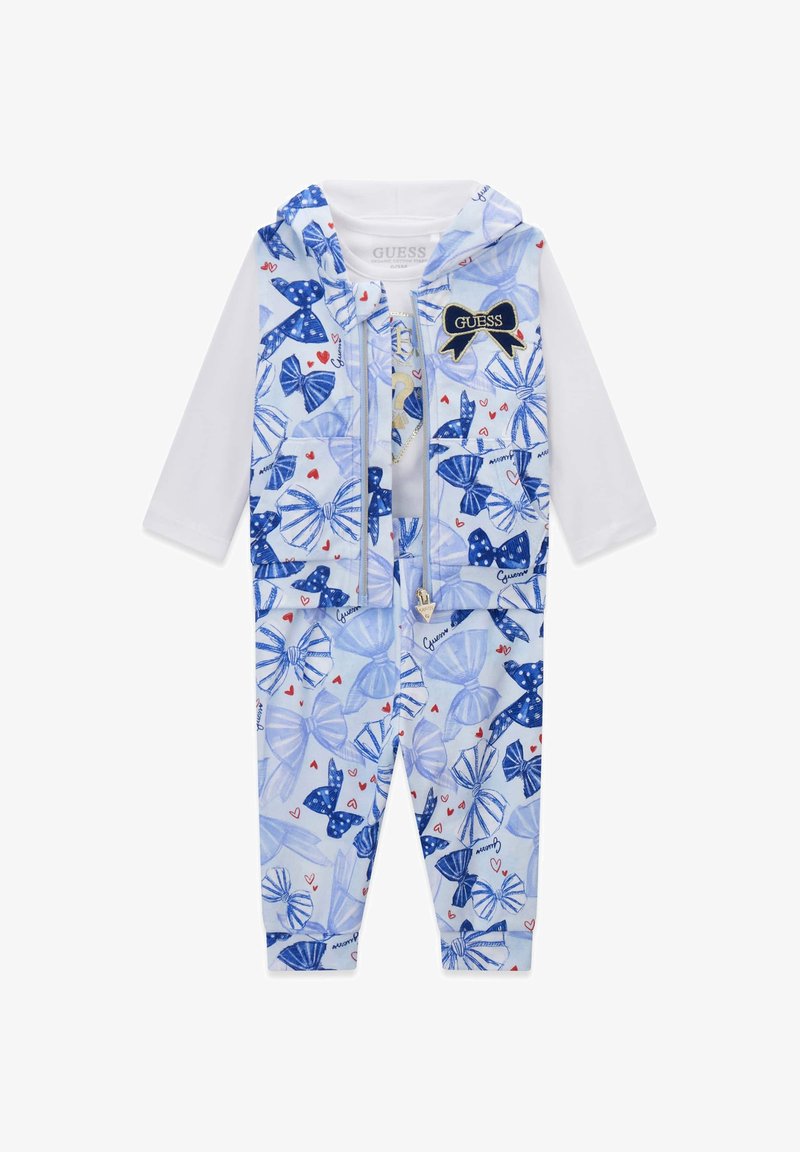 Haut blanc à manches longues avec un sweat à capuche sans manches à motifs de nœuds bleus et pantalon assorti, ornés de petits cœurs rouges et d'un écusson logo "Guess".