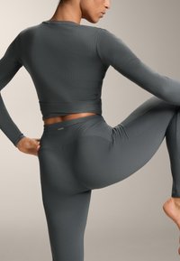 Prilagođena tamnosiva majica dugih rukava i odgovarajuće tajice visokog struka s rebrastom teksturom, koje prikazuju bešavni dizajn i naglašene šavove.