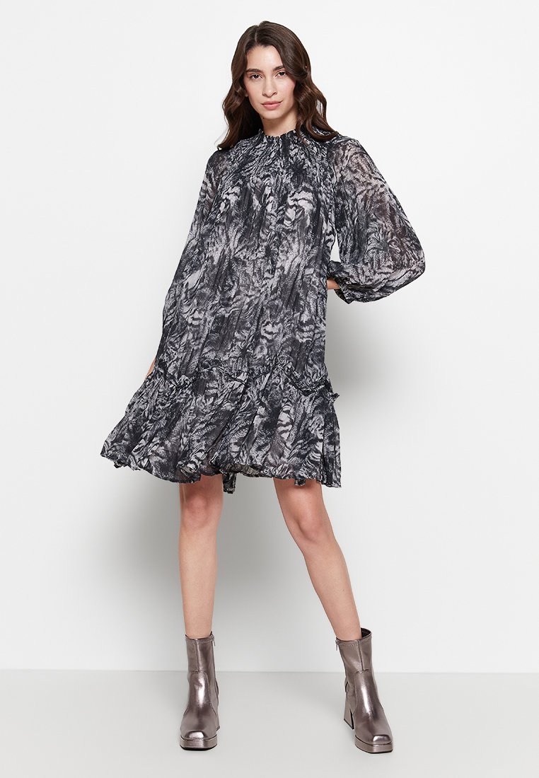 Zwart en grijs gemêleerde jurk met lange mouwen, een geraffineerde halslijn en een ruches zoom, gecombineerd met metalen enkellaarsjes.