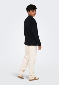 Svart langermet skjorte, avslappet passform, kombinert med kremfargede løse bukser og beige sneakers. Minimalistisk design, myk tekstur og uformelt utseende.