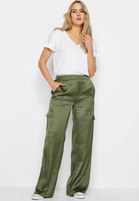 Olijfgroene satin cargo broek met zijzakken, hoge taille, losse pasvorm, gecombineerd met een witte V-hals t-shirt en witte sneakers.