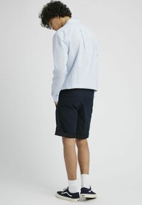 Chemise à manches longues rayée bleu clair et blanche, shorts marins, chaussettes blanches et baskets marines. Look décontracté avec un détail de pli au dos.