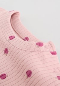 Tissu côtelé rose avec motif de tulipes violettes, doté d'un col rond et de boutons-pression le long de la couture d'épaule.