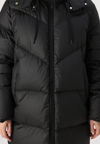 Black insulated puffer jacket with a zip front, chevron quilted texture, adjustable hood with drawstrings, and snap buttons at shoulders.