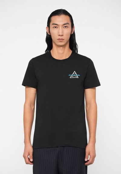 Melnā T-kreklus ar apaļu kakla izgriezumu, uz kuras kreisās krūtis ir balts un zils trīsstūra grafiskais attēls. Īsās piedurknes, kokvilnas materiāls.