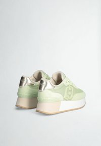 Sneakers verdi in suede e rete con accenti metallici, suola platform spessa bianca e un motivo decorativo sul tallone.